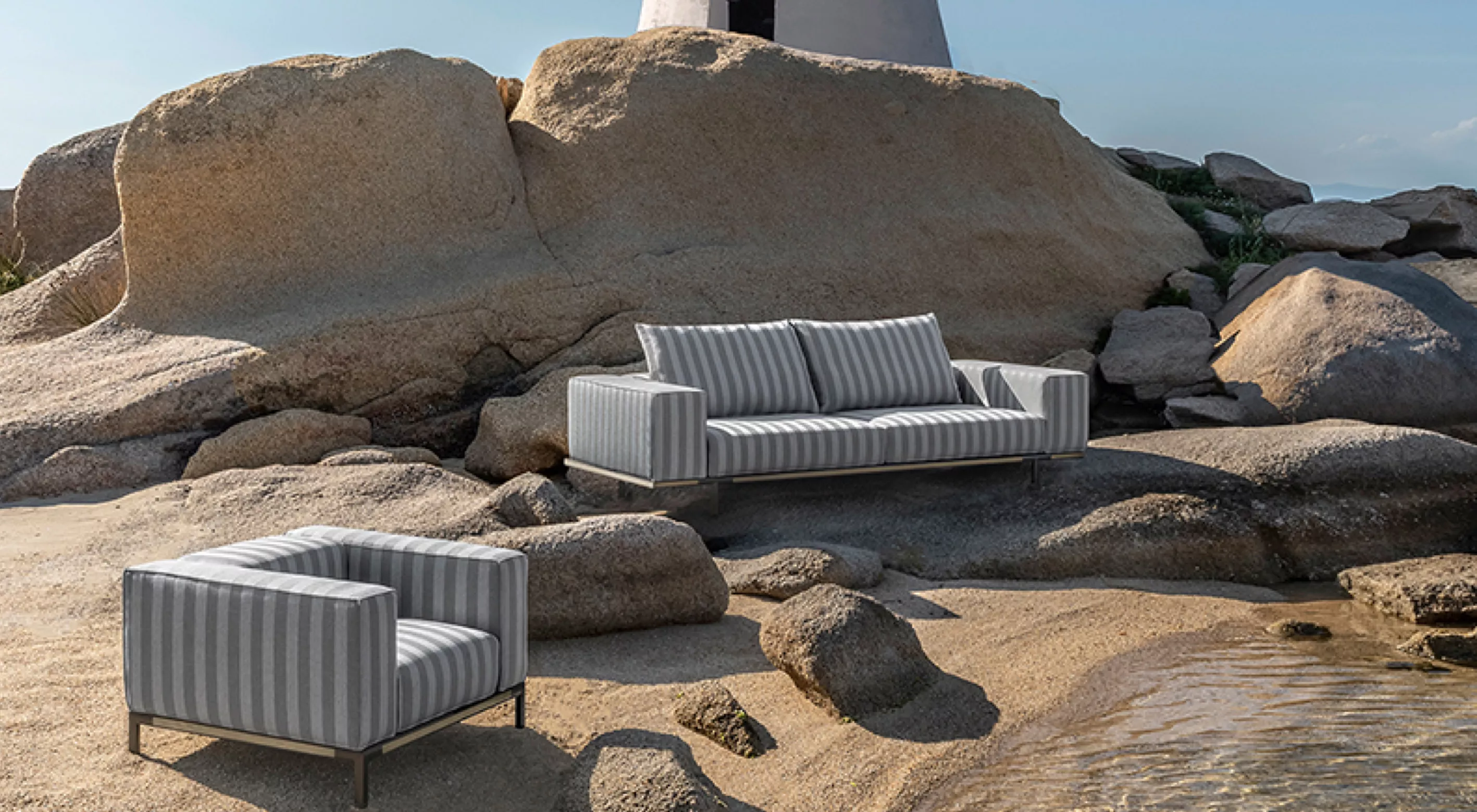Sofa und Sessel Costiera von Villa Schmidt in Grau-Weiß gestreift auf felsigem Strandhintergrund bei sonnigem Wetter.