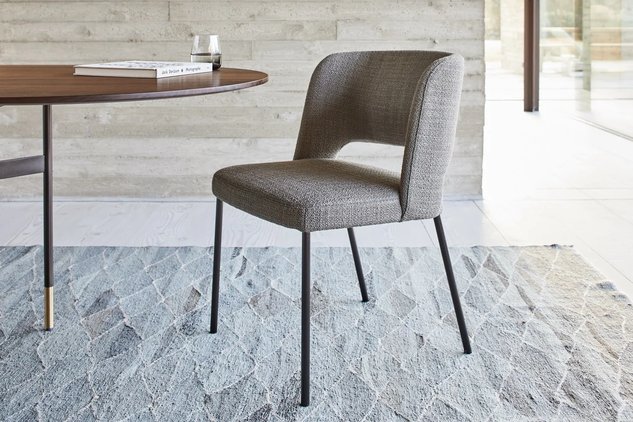 Grauer VS MORE HARRI Stuhl in modernem Wohnzimmer auf hellem Teppich, neben rundem Holztisch mit Glas und Buch.