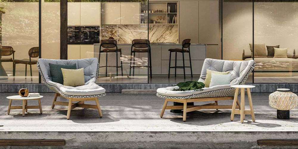 Zwei gemütliche, graue Outdoor-Sessel mit Kissen von Villa Schmidt auf einer Terrasse vor einer modernen Glasfassade.