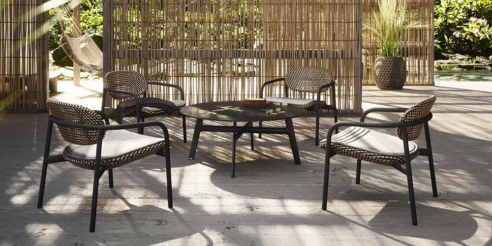 Dedon Roii Kollektion zeigt vier Stühle und einen Tisch in einem stilvollen Außenbereich mit Bambuswänden und Pflanzen im Hintergrund