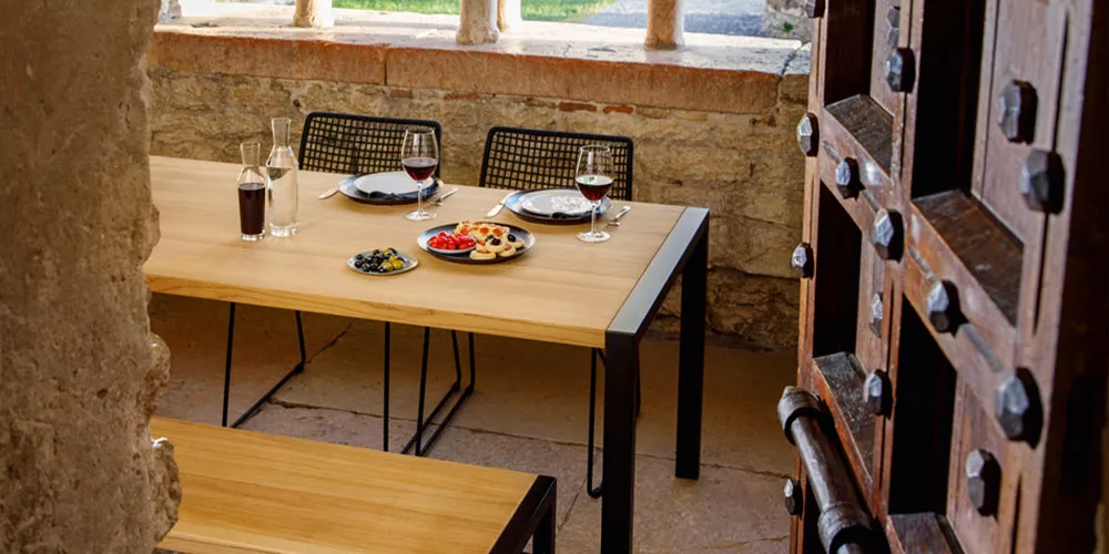 Weishäupl Flip Tisch in Holzoptik mit schwarzem Metallgestell, gedeckt mit Tellern und Gläsern, in rustikalem Innenhof.