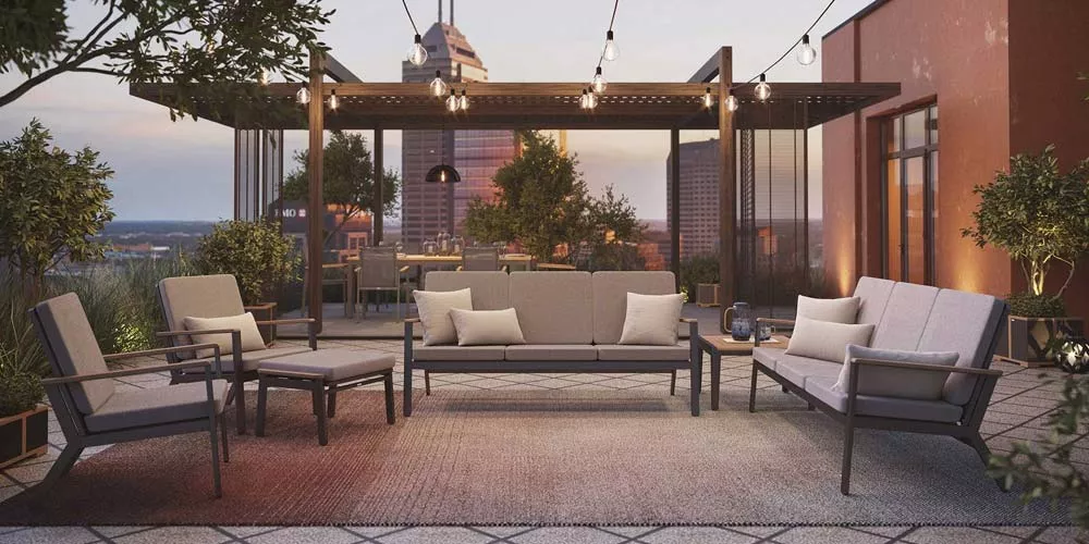 Barlow Tyrie Aura Lounge in Grau auf einer stilvollen Dachterrasse bei Sonnenuntergang, umgeben von Pflanzen und Lichterketten.