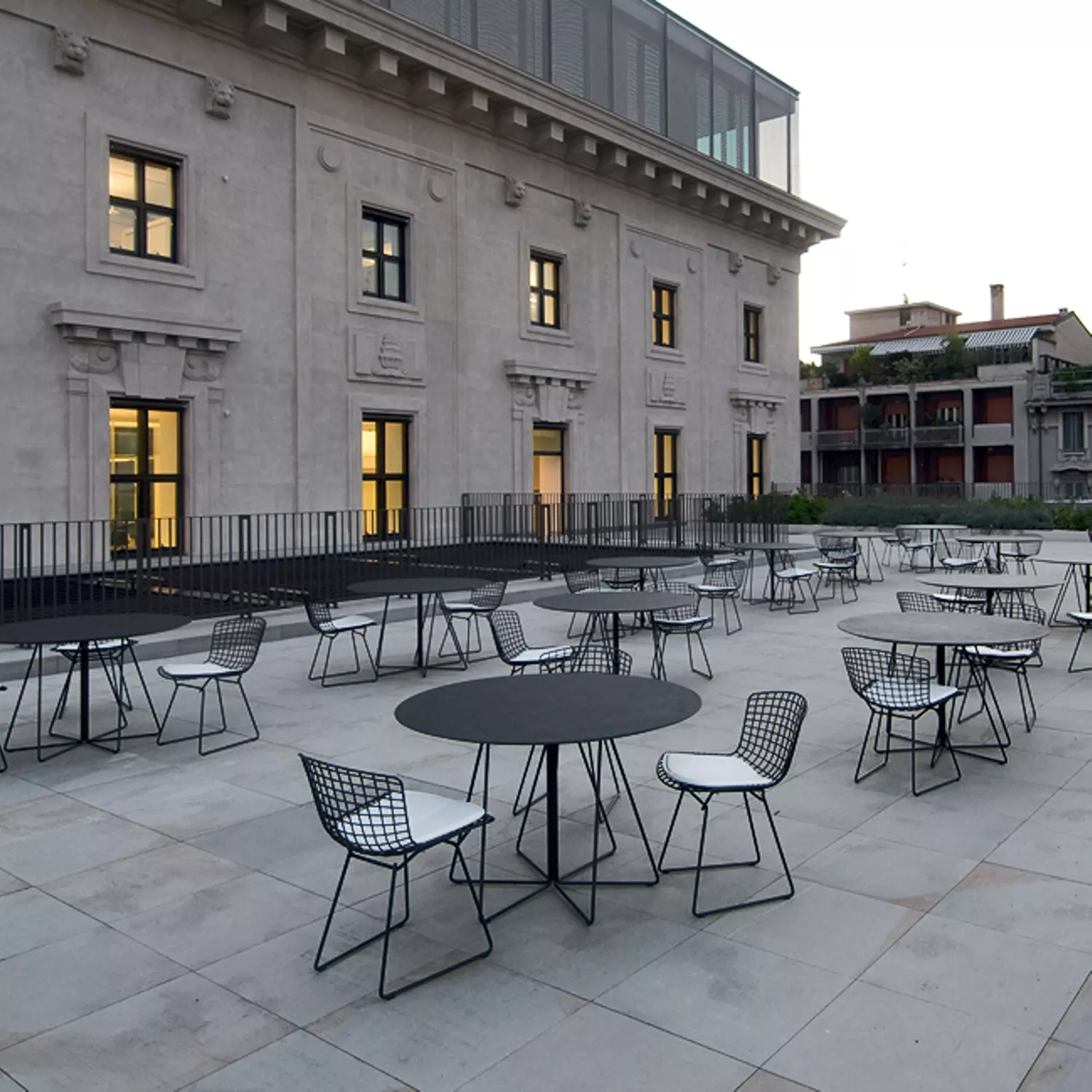Knoll Paperclip Outdoor Tisch mit Glasplatte 120 cm auf einer Terrasse vor einem großen Gebäude mit mehreren Tischen und Stühlen