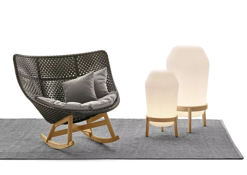 Dedon Loon Gartenleuchte und Bodenleuchte auf grauem Teppich neben einem geflochtenen Schaukelstuhl mit Kissen in einer gemütlichen Umgebung