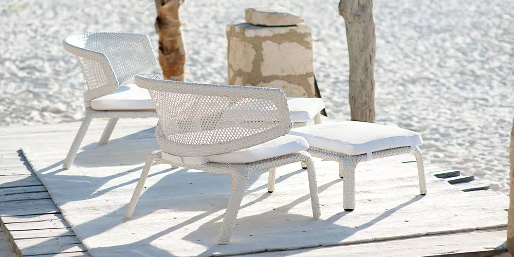 Zwei Dedon Seashell Stühle und Hocker stehen auf einer Holzplattform am Strand in einer entspannten Atmosphäre.