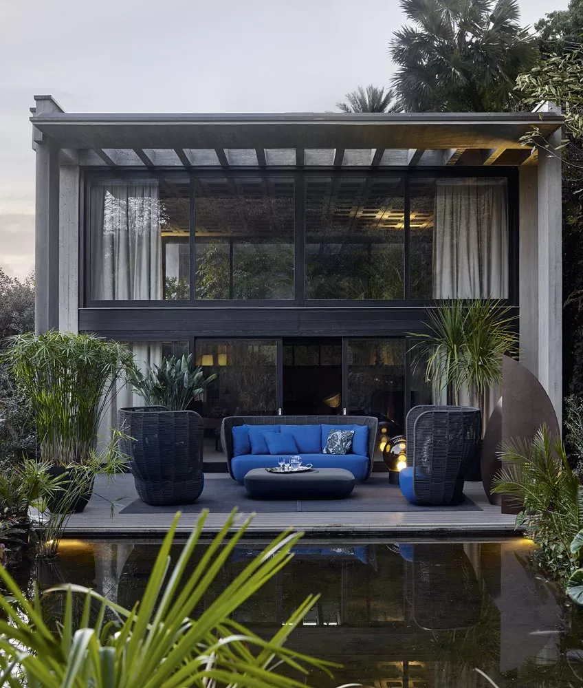 B&B Italia Bay Loungegruppe in einem modernen Garten vor einem stilvollen Haus mit großen Fenstern und üppiger Vegetation im Hintergrund