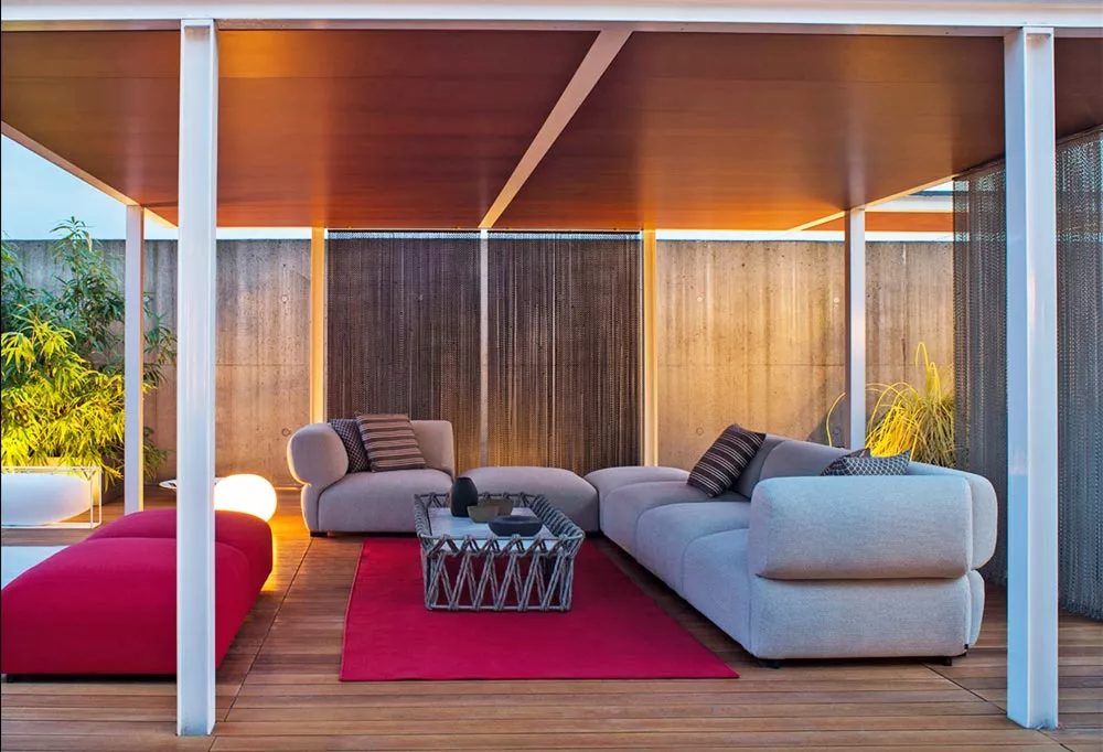 B&B Italia Butterfly Gartenmöbel Loungegruppe auf einer Terrasse mit Holzboden und moderner Überdachung bei Abenddämmerung mit Pflanzen im Hintergrund