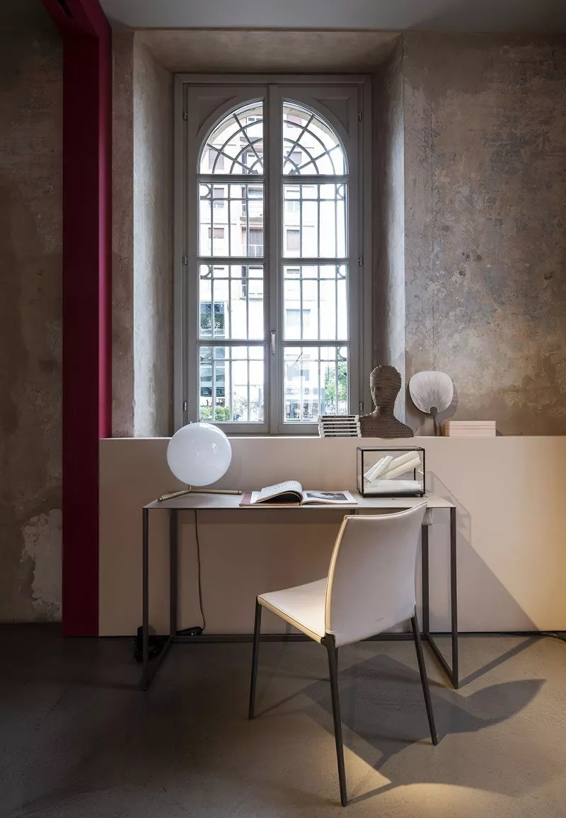 Zanotta Lia Stuhl in einem modernen Arbeitszimmer mit Schreibtisch Lampe und Dekoration vor einem Fenster mit Gitter in einem industriellen Raum.