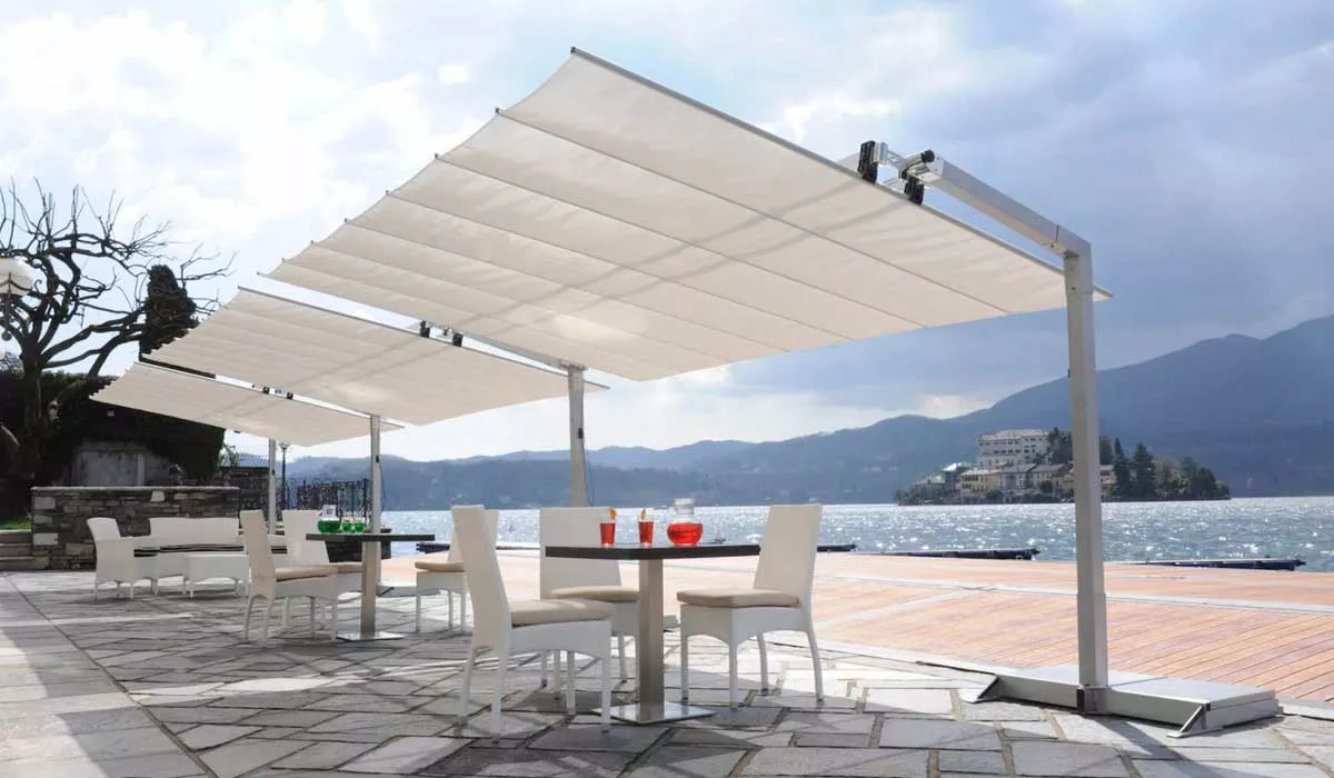 FIM Flexy Sonnenschirme in Weiß, aufgestellt auf einer Terrasse mit Seeblick, umgeben von Tischen und Stühlen, bei bewölktem Himmel.