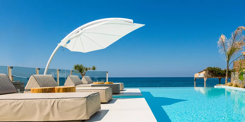 Sonnenschirm Icarus von Villa Schmidt in Weiß, auf einer Terrasse mit Pool und Meerblick, bei strahlend blauem Himmel.