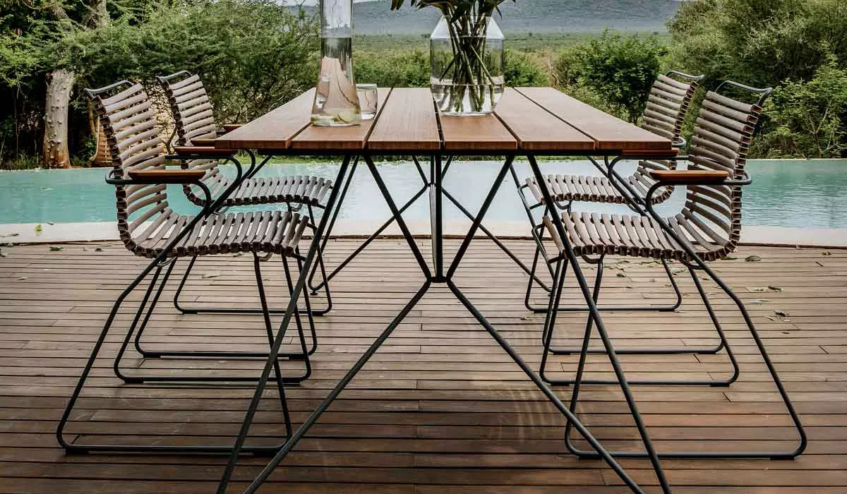 Houe Sitzmöbel in Braun und Schwarz, aufgestellt auf einer Holzterrasse mit Pool und grüner Landschaft im Hintergrund.