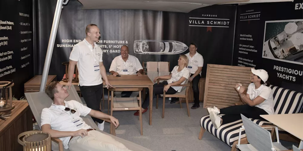 Personen in einem Ausstellungsraum von Villa Schmidt, umgeben von hochwertigen Gartenmöbeln und Yachtdesigns, in entspannter Atmosphäre.