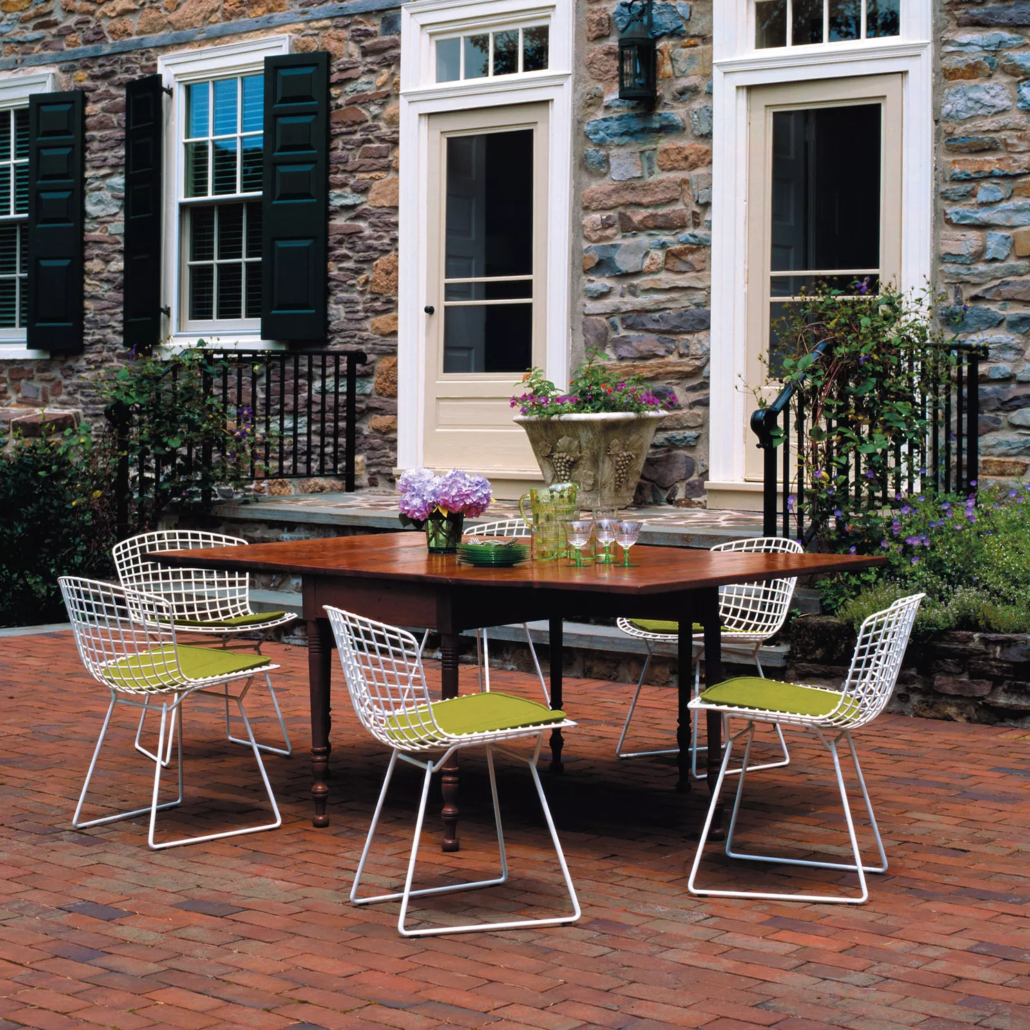 Knoll Harry Bertoia Outdoor Stuhl weiß auf einer Terrasse mit einem Holztisch und Blumenarrangement im Freien