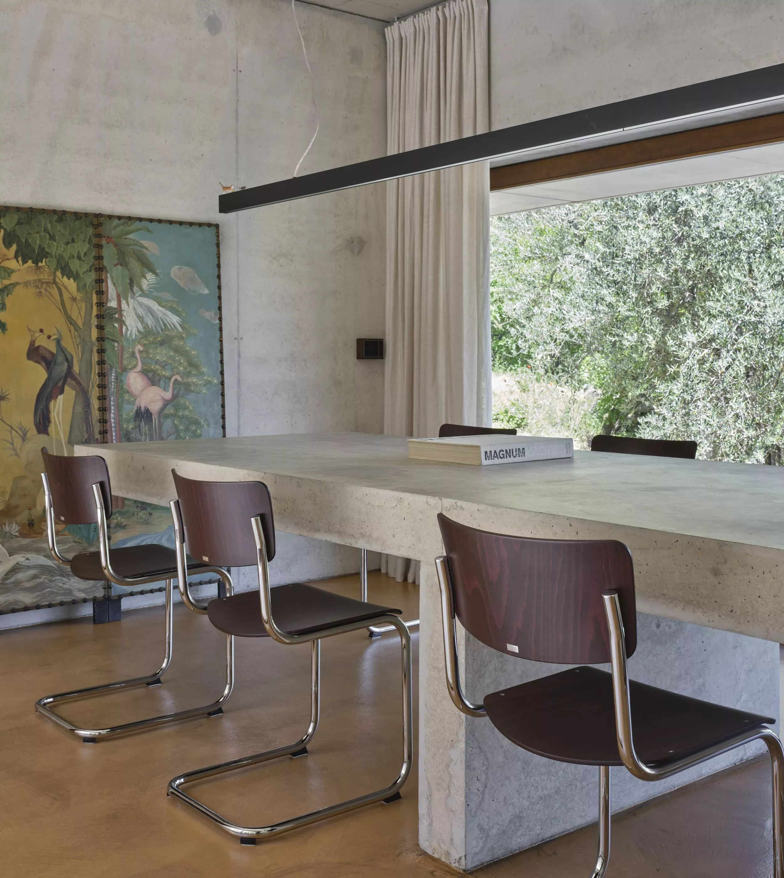 Thonet Stühle an einem Beton Esstisch in einem modernen Raum mit großen Fenstern und einem Gemälde im Hintergrund