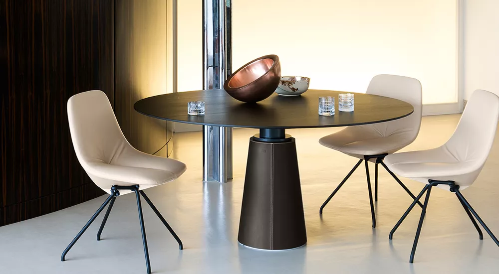 Runder Tisch von Potocco, Modell Mesa Due, in Schwarz mit kupferner Schale, umgeben von beigen Stühlen, auf hellem Boden.