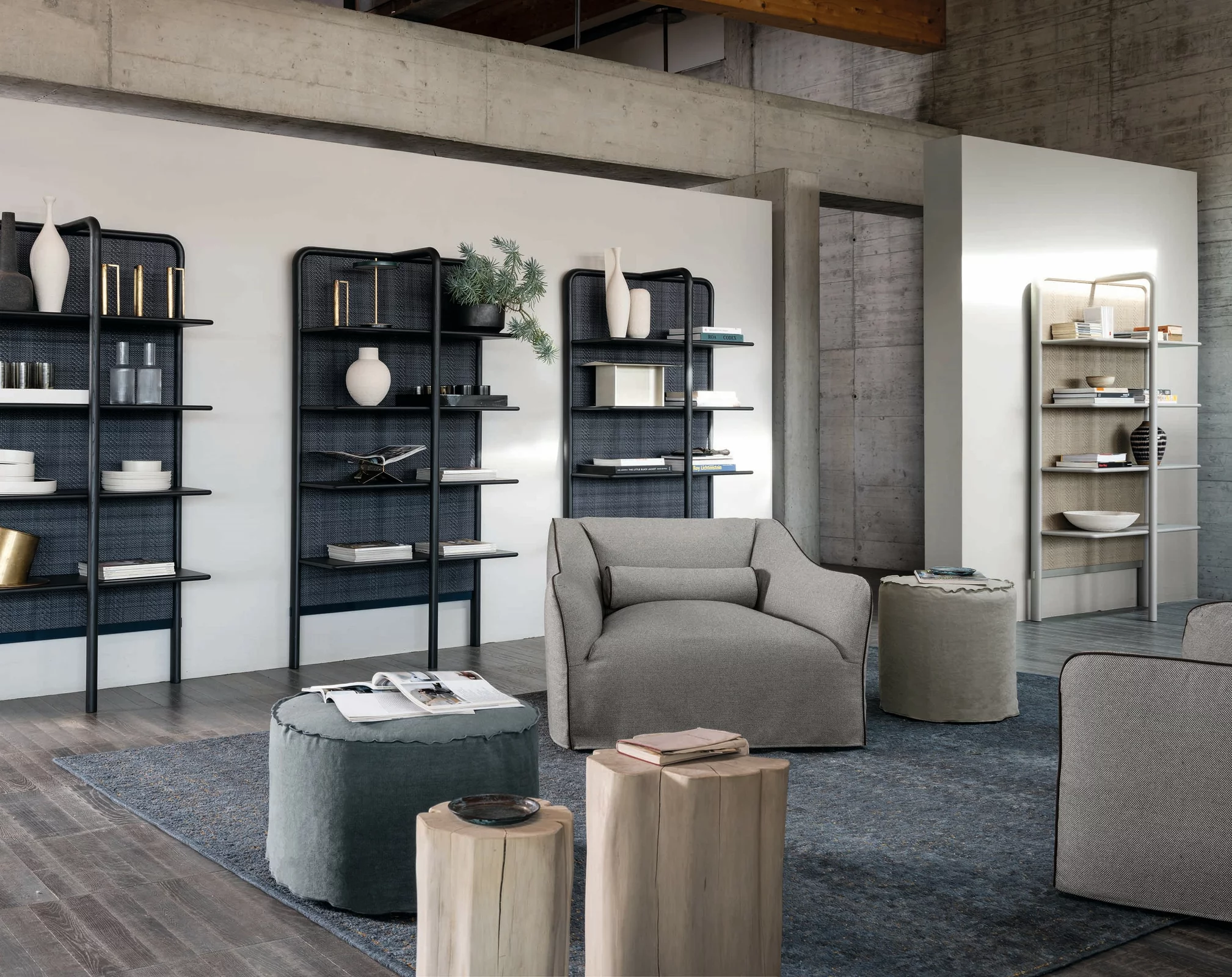 Gervasoni Kollektion 2023 Wohnzimmer mit grauem Sessel und Hocker vor Bücherregalen mit Dekorationen und Holzdetails in modernem Ambiente