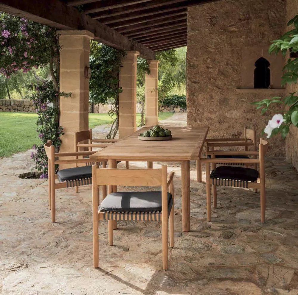 Dedon Tibbo Essgruppe aus hellem Holz mit schwarzen Sitzkissen auf einer rustikalen Steinterrasse im Freien.