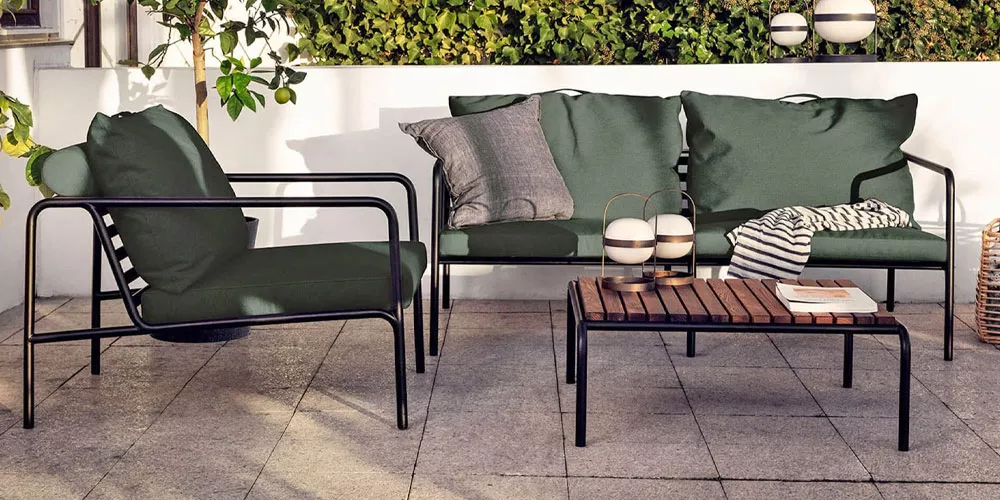 Gartenmöbel-Set von Houe, Kollektion Avon, in Dunkelgrün mit schwarzem Metallrahmen, bestehend aus Sofa, Sessel und Tisch auf einer Terrasse.