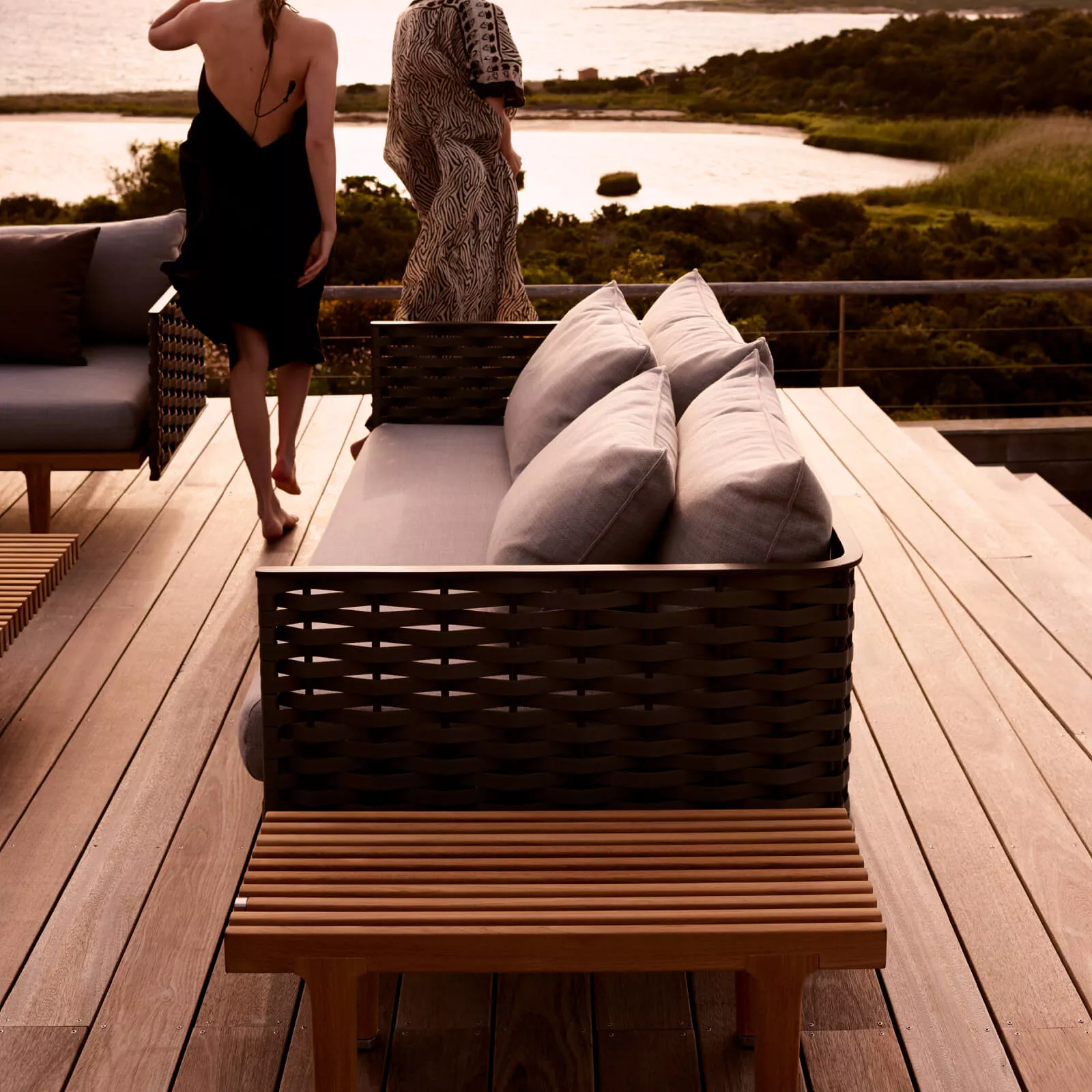 Zwei Frauen entspannen auf einer Dedon Sealine Lounge auf einer Terrasse mit Blick auf einen See und grüne Landschaft im Hintergrund.