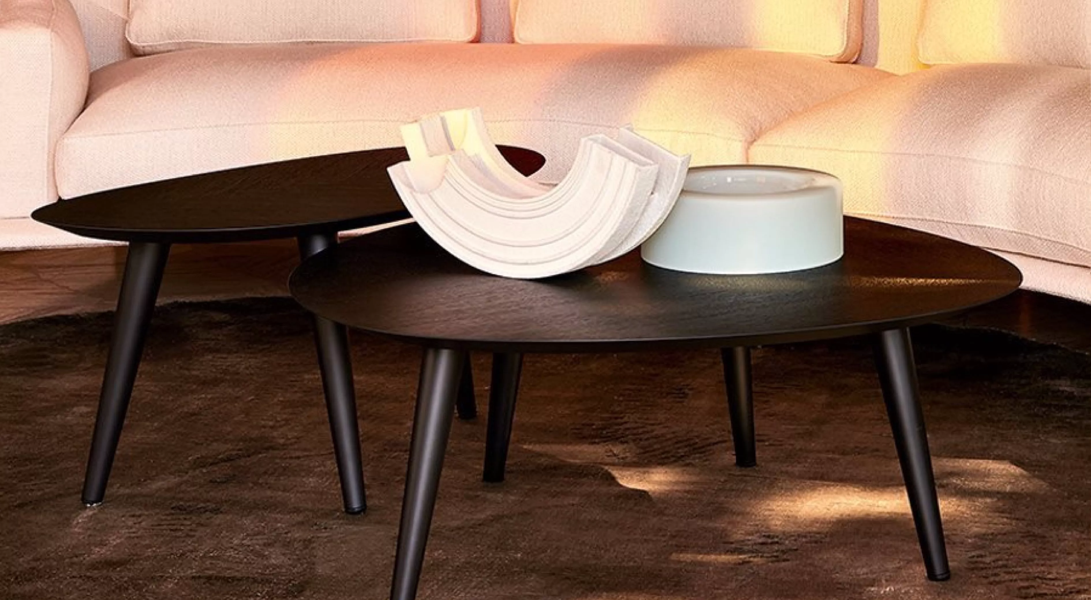 Zwei schwarze Tweed Mini Couchtische auf einem braunen Teppich vor einem beigen Sofa, dekoriert mit einer weißen Skulptur und einer blauen Schale.