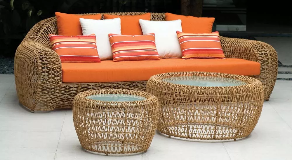 Kenneth Cobonpue Balou Sofa in Orange mit passenden runden Rattan-Couchtischen, auf einer Terrasse mit Steinboden, stimmungsvolles Bild.