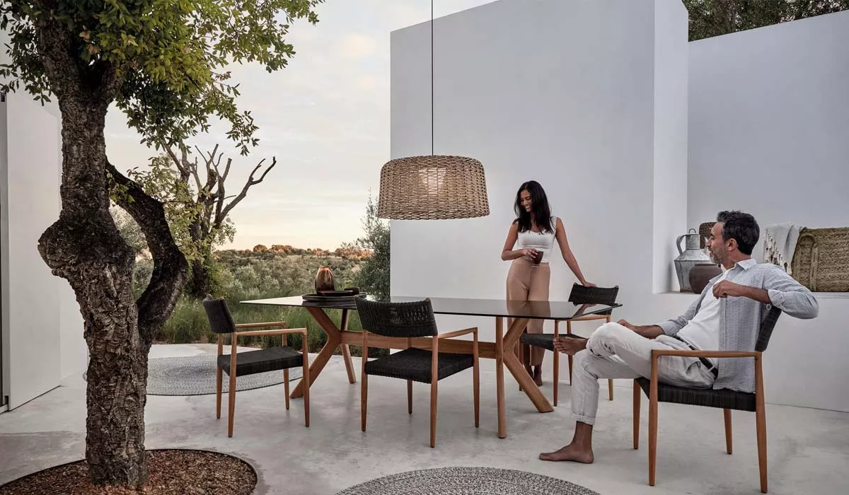 Gloster Frame Gartenmöbel Essgruppe in modernem Design mit Holztisch und Stühlen auf einer Terrasse, umgeben von Natur.