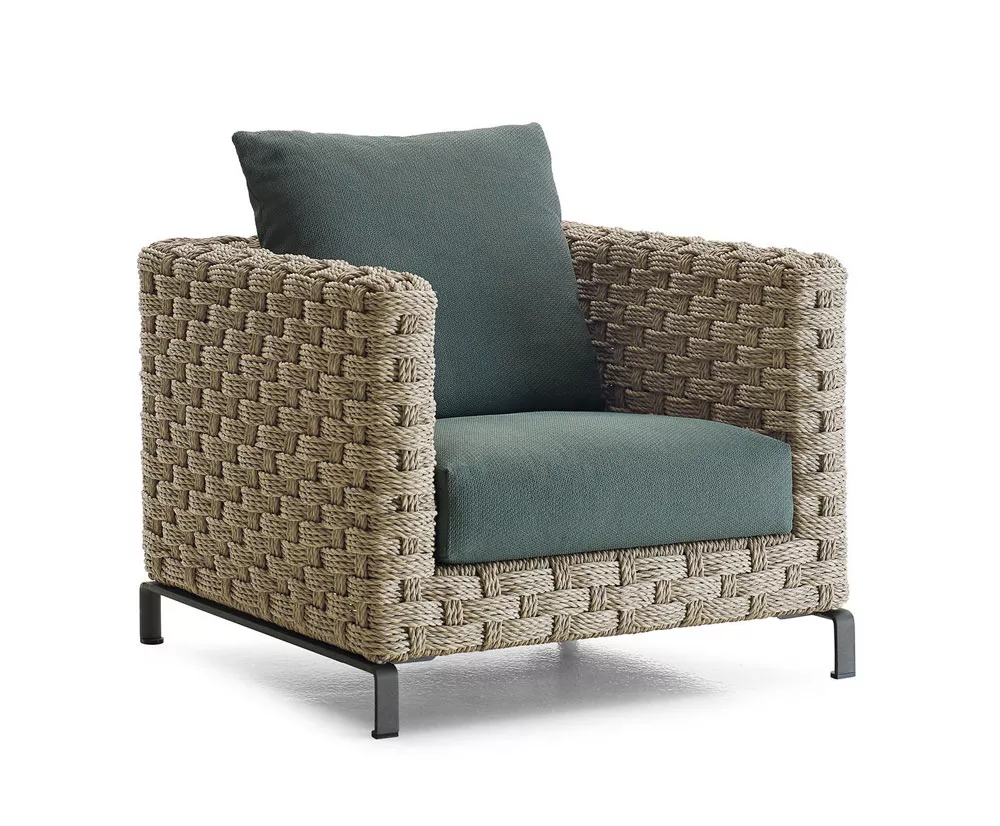 B&B Italia Ray Outdoor Natural Loungesessel 85 cm in einem Moodbild mit grünem Kissen und geflochtenem Design auf einem weißen Hintergrund.