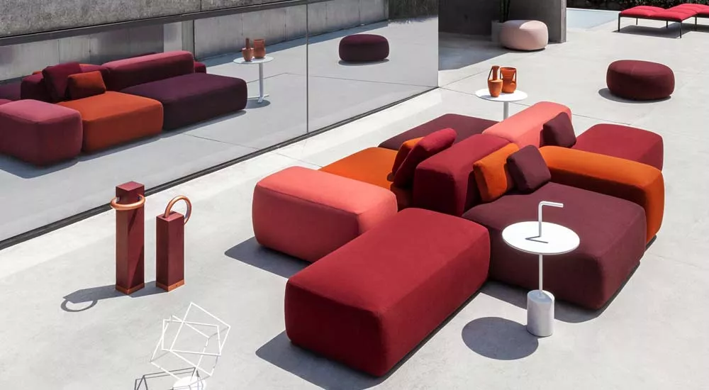 Lapalma PLUS Outdoor Loungegruppe in Rot- und Orangetönen auf einer modernen Terrasse mit Betonboden und Glaswand im Hintergrund.