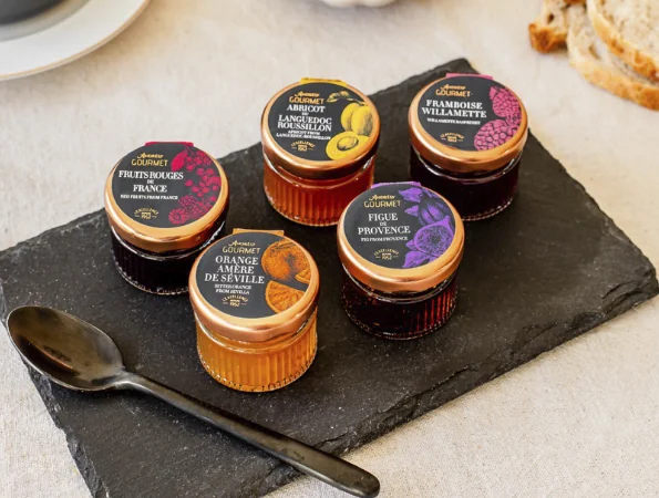 Fünf Gläser Andresy Konfitüren in verschiedenen Geschmacksrichtungen auf einer Schieferplatte, mit einem Löffel im Vordergrund.