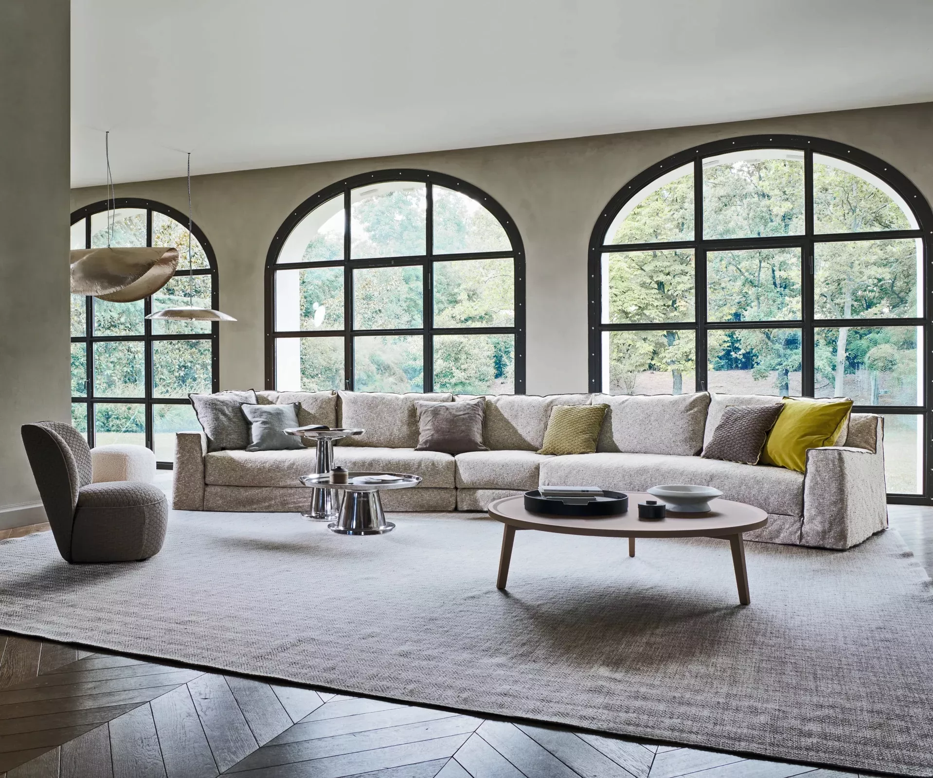 Graues Loll Next Nuvola Sofa in modernem Wohnzimmer mit großen Fenstern, Holzboden und stilvollen Beistelltischen.