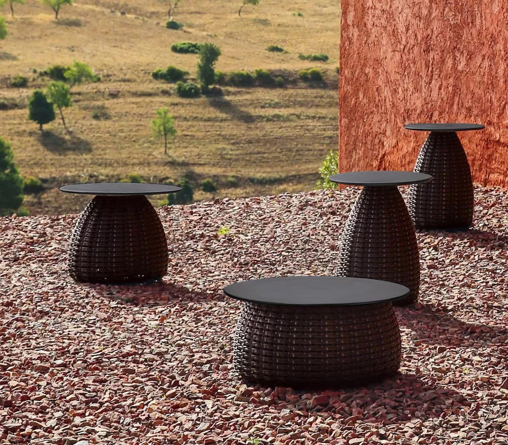 Dedon Porcini Beistelltisch in einer Außenaufnahme auf einer Kiesfläche mit Landschaft im Hintergrund