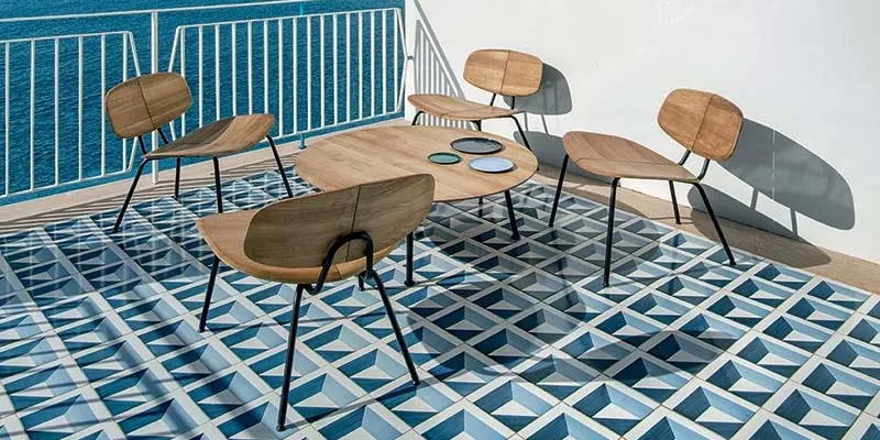 Ethimo Agave Outdoor Loungegruppe in Holzoptik auf blau-weiß gemustertem Balkonboden mit Meerblick im Hintergrund.