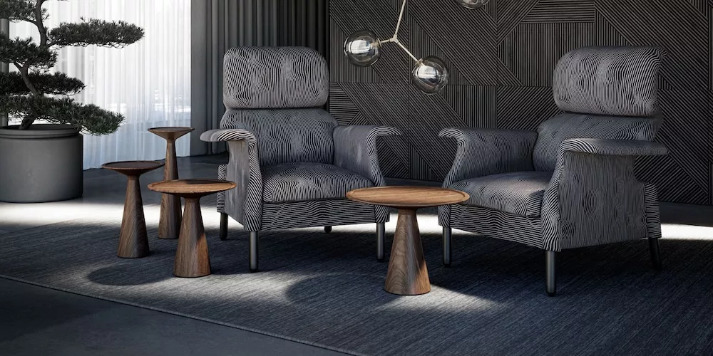 Zwei graue Sessel und drei hölzerne Beistelltische von Draenert in einem modern eingerichteten Wohnzimmer mit Teppich und Pflanzen im Hintergrund