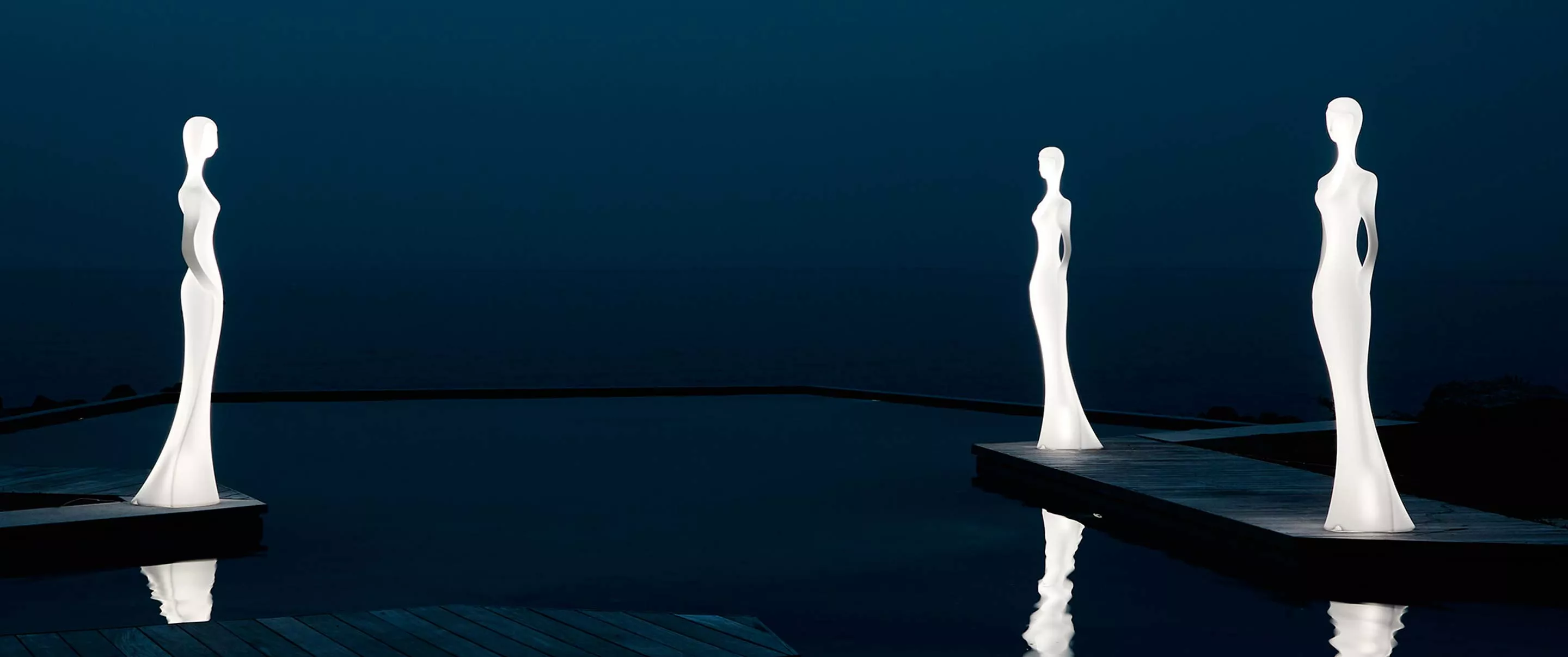 Zwei weiße Myyour Penelope Leuchten stehen auf einem Steg vor einem dunklen, ruhigen Wasserhintergrund bei Nacht.