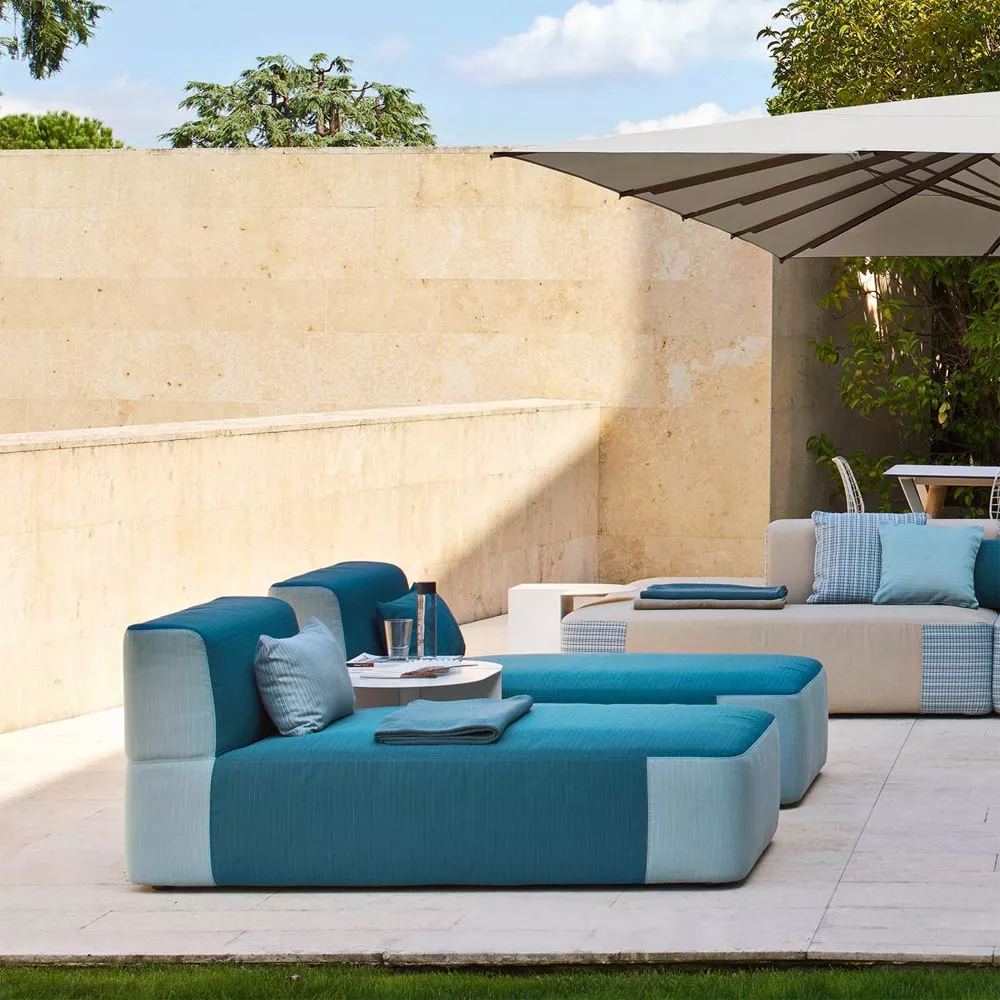 Varaschin Belt Daybed Loungesofa in Blau, 160 cm, auf einer sonnigen Terrasse mit Steinmauer und Sonnenschirm im Hintergrund.