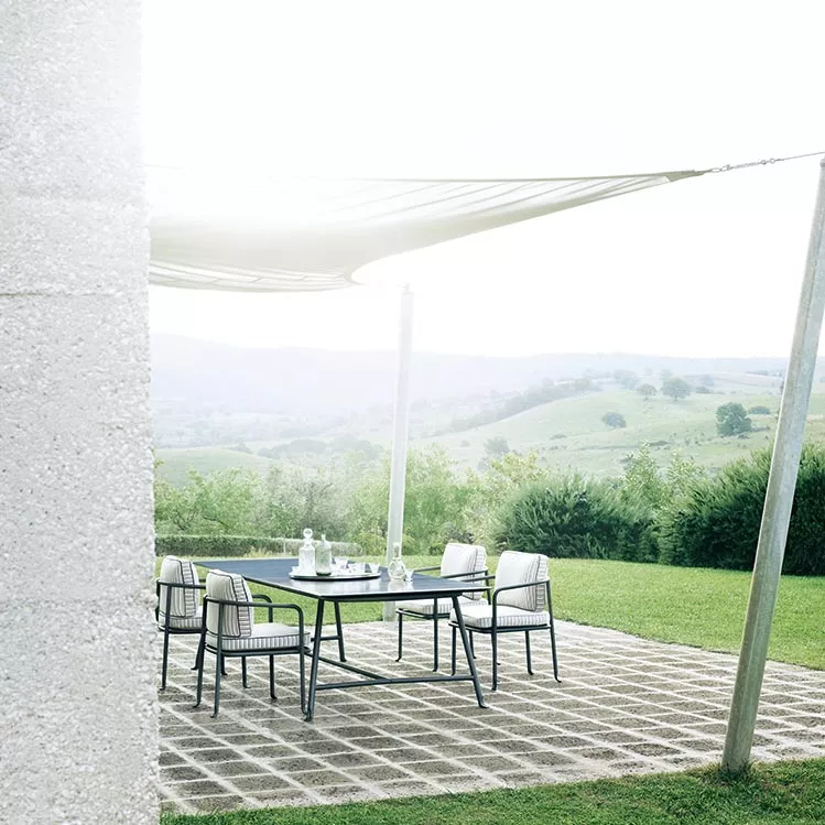 B&B Italia Borea Essgruppe auf einer Terrasse mit Blick auf eine grüne Landschaft und einem Sonnensegel im Hintergrund