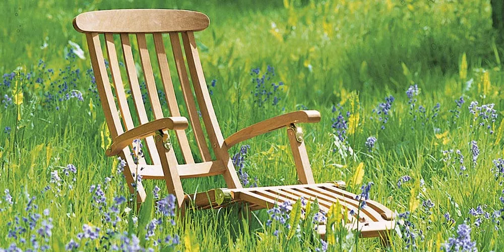 Barlow Tyrie Commodore Liegestuhl aus Teakholz in einer blühenden Wiese, seitliche Ansicht.