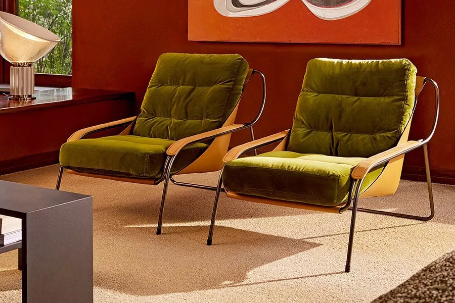 Zwei grüne MAGGIOLINA Sessel mit Metallrahmen und Holzarmlehnen auf beigem Teppich vor einer roten Wand in einem modernen Wohnzimmer.