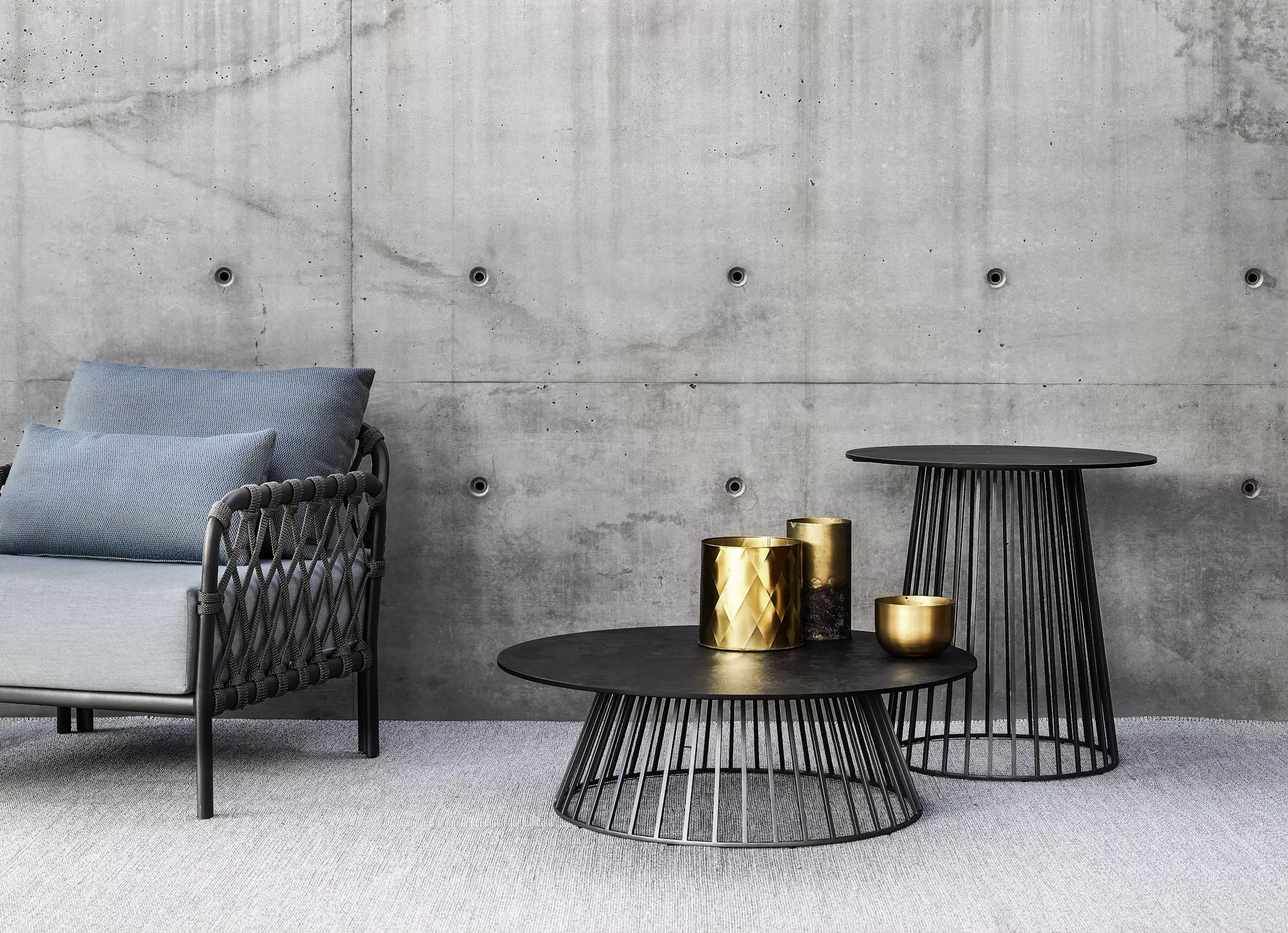 Solpuri Grid Lounge Sessel mit blauen Kissen und zwei schwarzen Beistelltischen mit goldenen Dekorationsobjekten vor einer Betonwand in einer modernen Umgebung