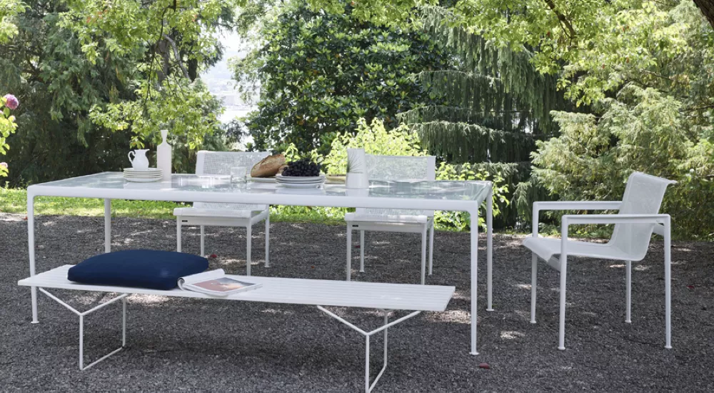 Gartenmöbel-Set von Villa Schmidt, bestehend aus einem weißen Tisch und Stühlen, auf Kiesboden vor grüner Waldkulisse.