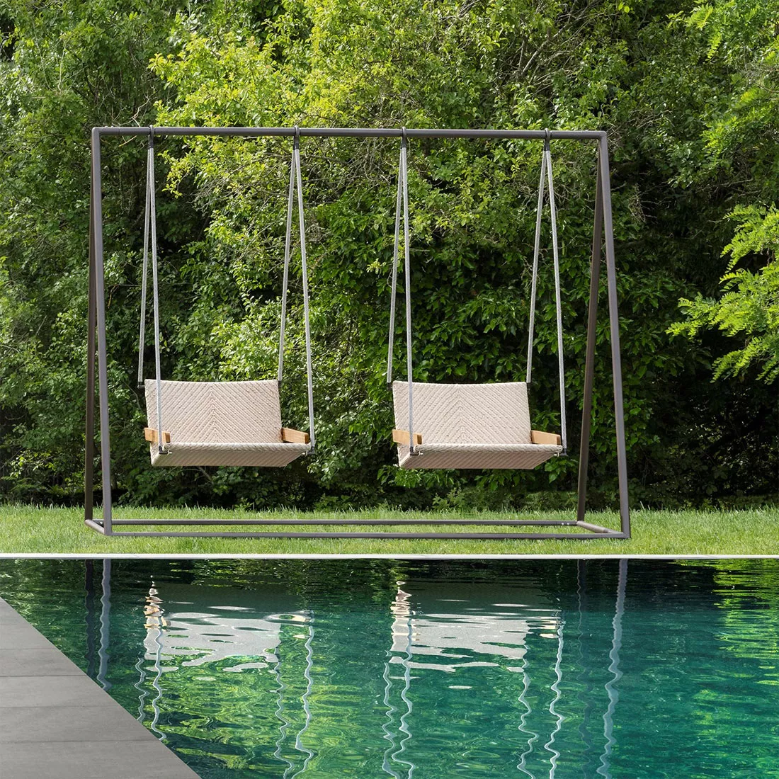 Zweisitzige Ethimo Allaperto Nautic Gartenschaukel aus Teakholz und Flat Rope vor grünem Gartenhintergrund am Pool.