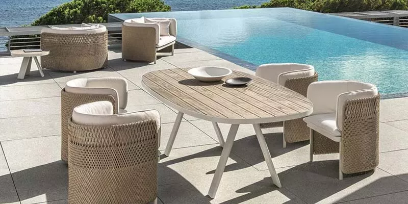 Ethimo Esedra Outdoor Ess-Loungegruppe in Beige und Weiß auf einer Terrasse mit Meerblick, bestehend aus Tisch und Sesseln.