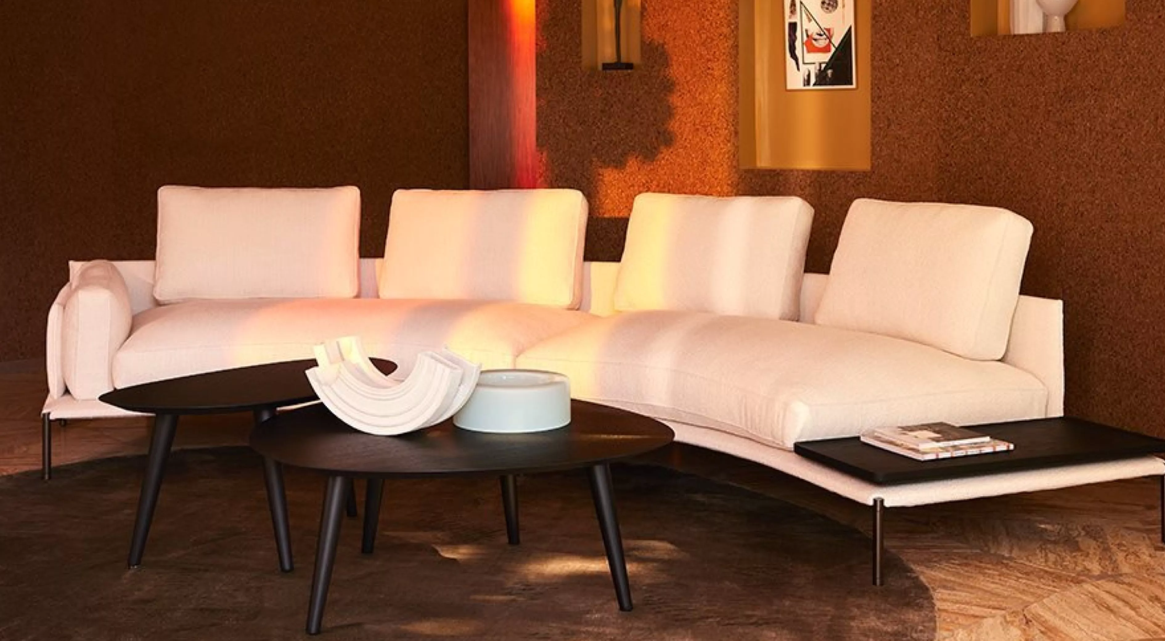 Ein elegantes Wohnzimmer mit einem cremefarbenen Noah-Sofa und zwei schwarzen Nickel-Couchtischen auf einem Holzboden vor einer warmen Wand.