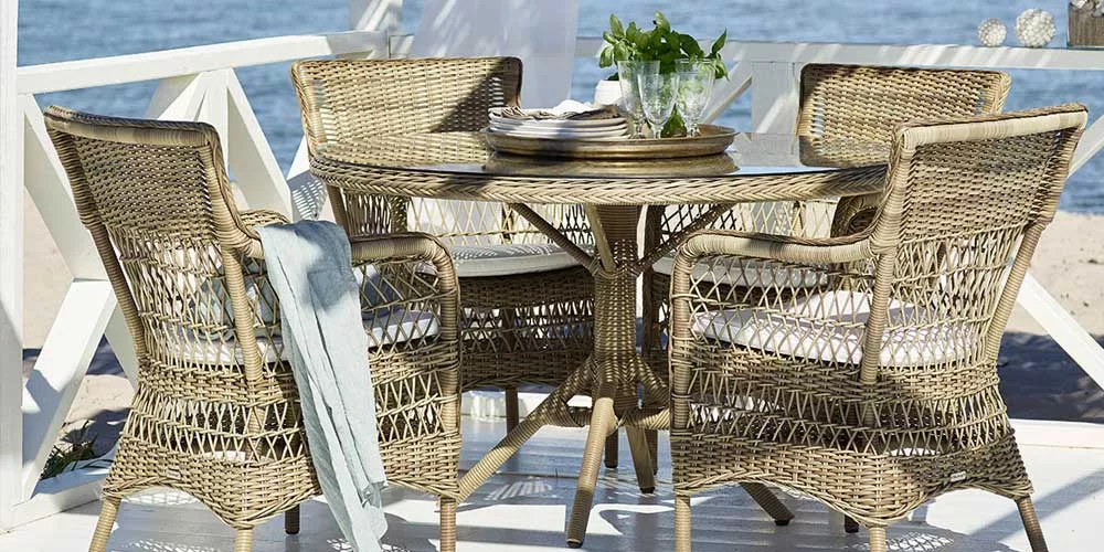 Sika-Design Marie Essgruppe aus Rattan in Naturfarbe auf einer Terrasse mit Meerblick, bestehend aus einem runden Tisch und vier Stühlen.