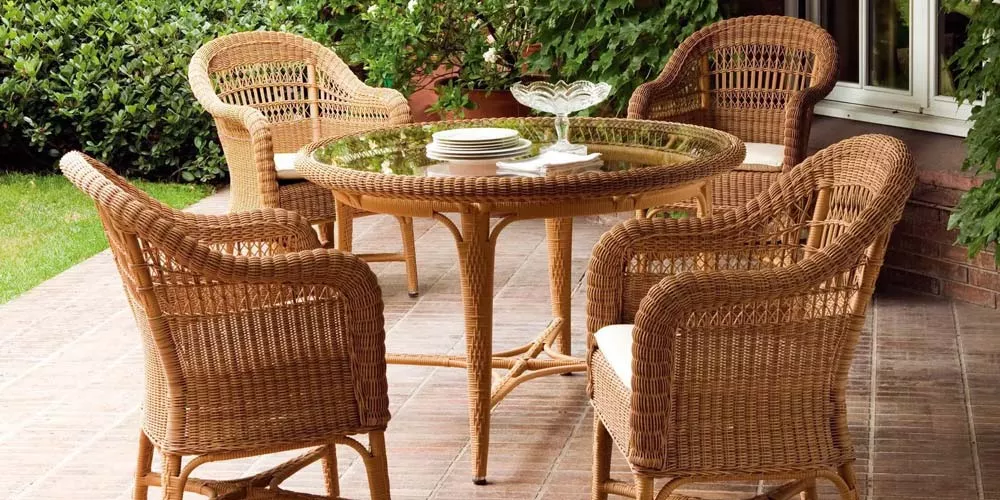 Point Alga Outdoor Essgruppe in Naturfarbe auf einer Terrasse mit vier Rattanstühlen und einem runden Tisch, umgeben von grünen Pflanzen.