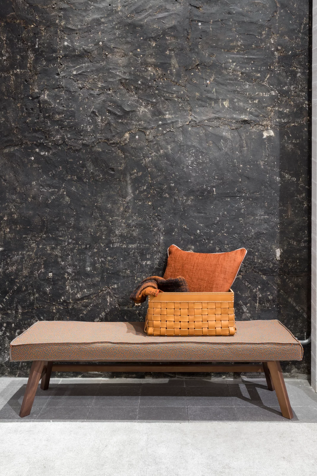Gervasoni Bank mit Kissen und Korb auf einer Bank vor einer dunklen Wand in einem modernen Raum