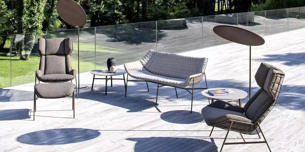 Varaschin Summerset Lounge Gartenmöbel in Grau auf einer Terrasse mit Glasgeländer und grünem Hintergrund, bestehend aus Sesseln und Sofa.