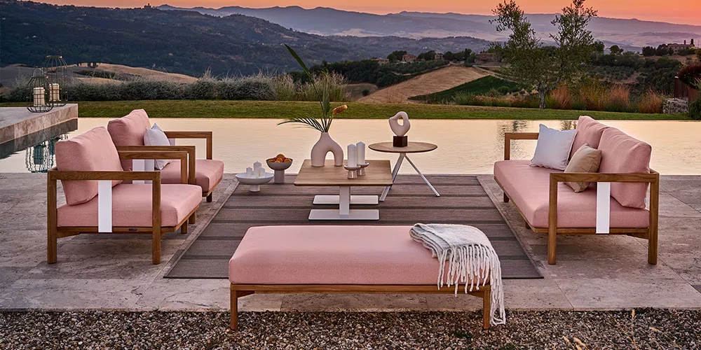 Weishäupl New Hampton Lounge-Set in Rosa auf einer Terrasse mit Blick auf die Landschaft bei Sonnenuntergang, bestehend aus Sofas und Tisch.