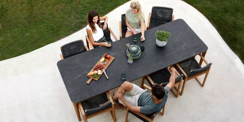 Draufsicht auf Cane-line Aspect Esstisch in Schwarz mit vier Personen, gedeckt mit Geschirr und Snacks, auf einer Terrasse.