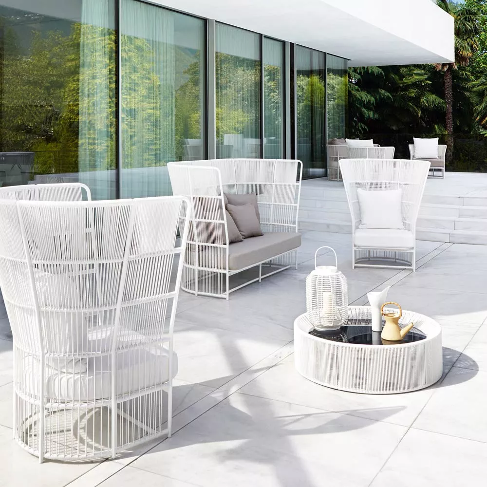 Varaschin Tibidabo Beistelltisch in Weiß auf einer modernen Terrasse mit Glasfassade und grüner Gartenkulisse.